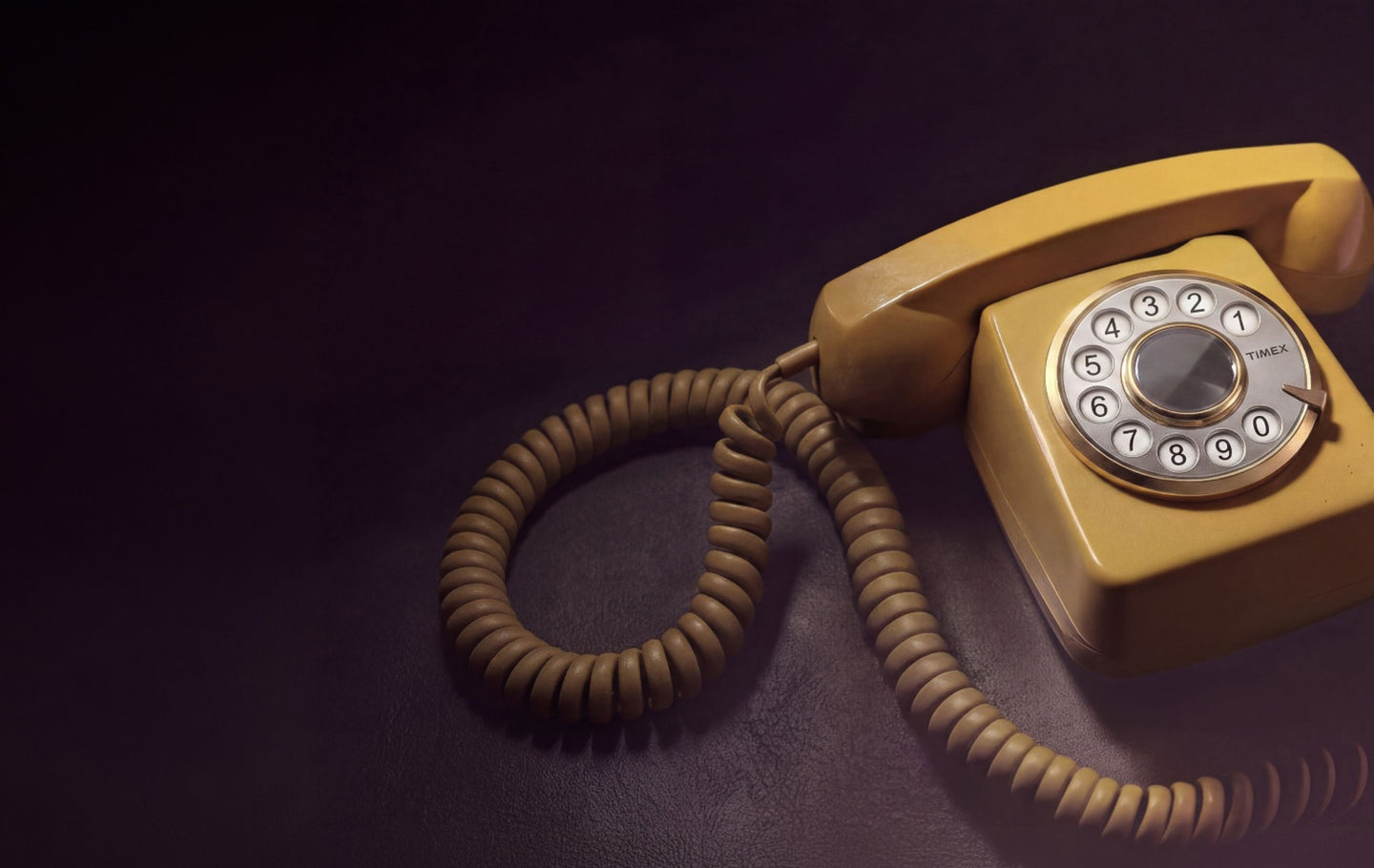 Teléfono antiguo de disco con un dial de la marca Timex expuesto sobre una superficie oscura, con un cable en espiral y una cálida iluminación retro.