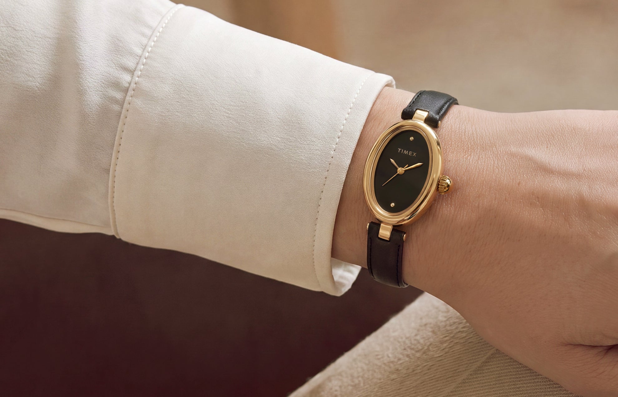 Primer plano del Timex Cavatina® Luxe con caja ovalada en tono dorado, esfera negra y correa de piel negra, lucido en la muñeca.