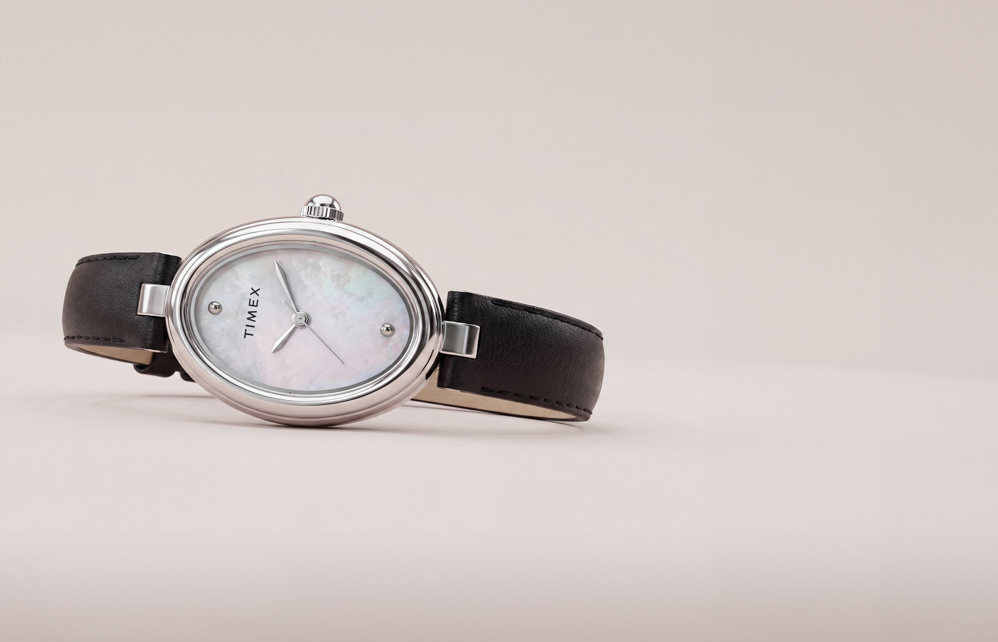 Reloj Timex Cavatina® Luxe con caja ovalada en tono plateado, esfera de nácar y correa de piel negra, presentado sobre un fondo suave y neutro.