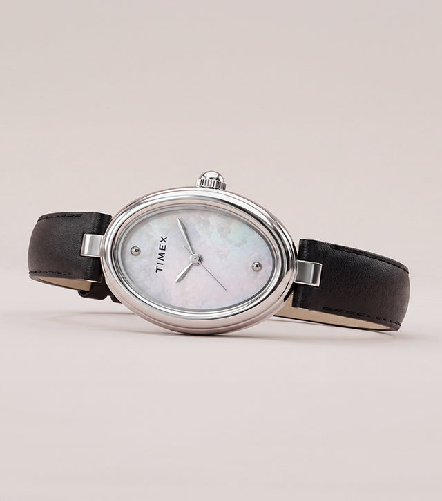 Reloj Timex Cavatina® Luxe con caja ovalada en tono plateado, esfera de nácar y correa de piel negra, presentado sobre un fondo suave y neutro.
