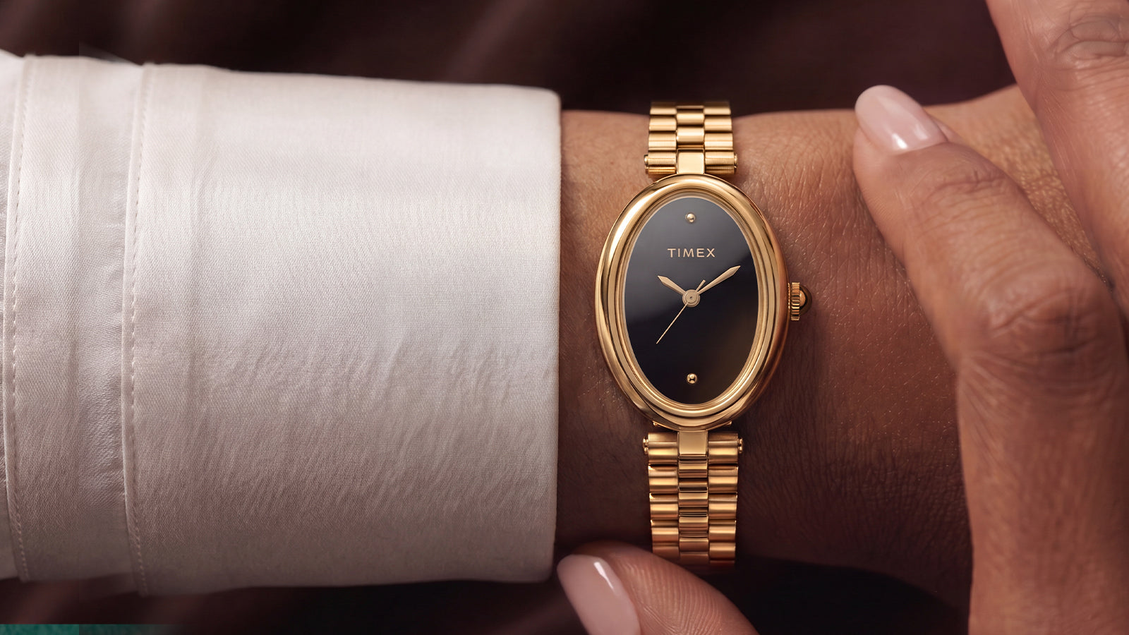 Timex Cavatina® Luxe gold-tone watch with a black dial and stainless steel bracelet worn on the wrist with a white cuff.