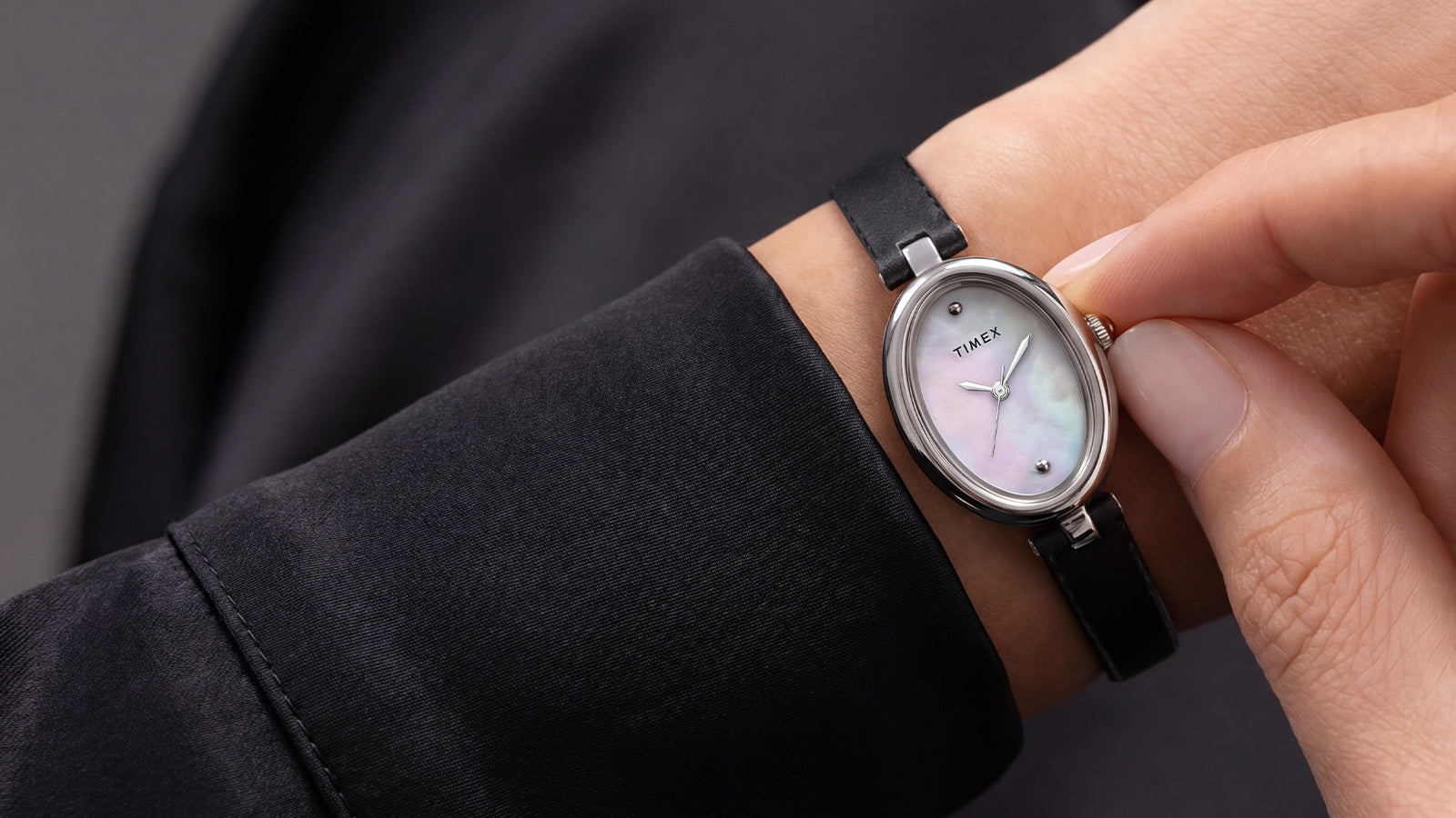 Primer plano del Timex Cavatina® Luxe con caja ovalada en tono plateado, esfera de nácar y correa de piel negra, puesto en la muñeca.