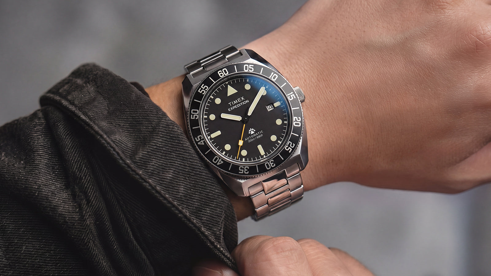 Close-up of the Timex Expedition Pioneer Automatic on a wrist, featuring a black dial, black rotating bezel, luminous markers, and stainless-steel bracelet.
