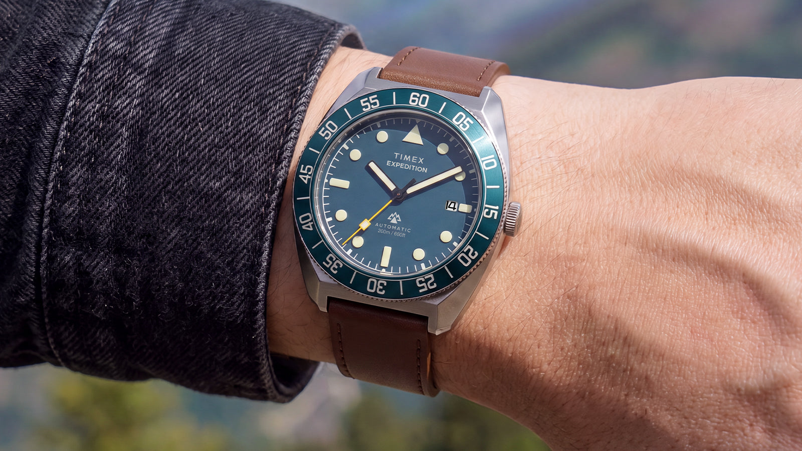 Close-up of the Timex Expedition Pioneer Automatic on a wrist, featuring a blue dial, blue rotating bezel, and brown leather strap.