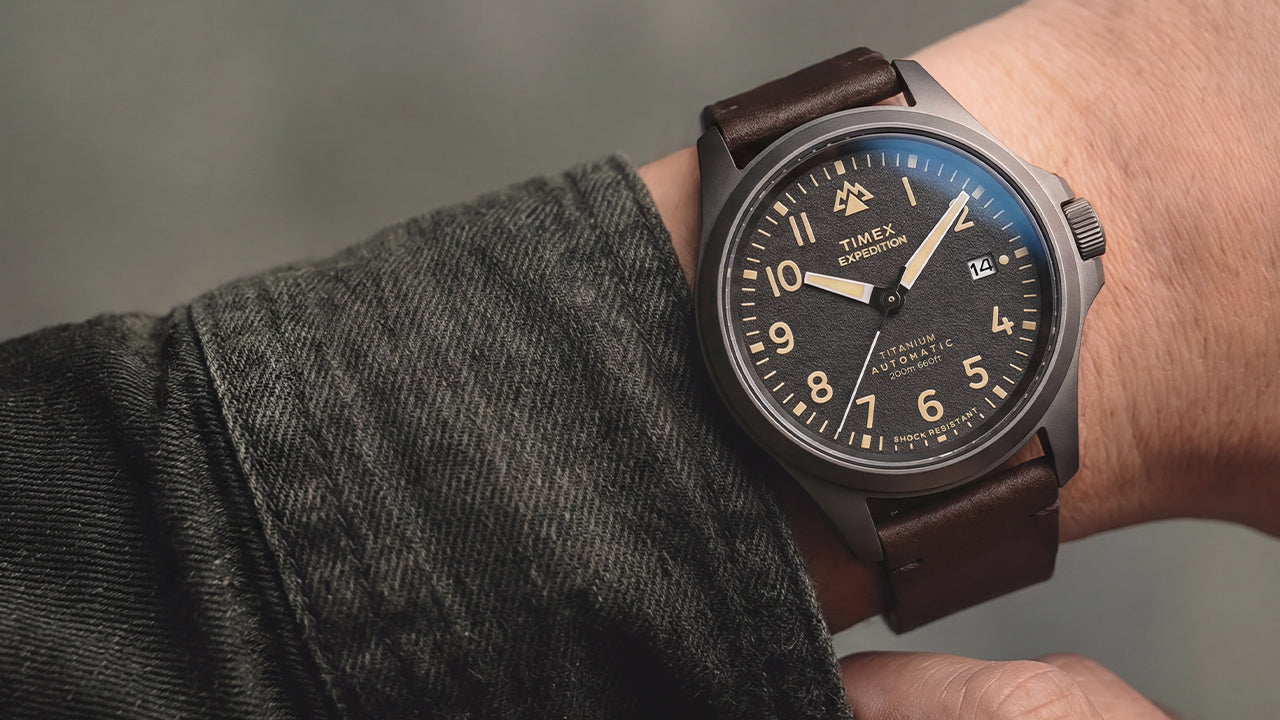 Expedition® Field Post Automatic titanium watch with a brown leather strap worn on the wrist, showcasing the black textured dial.