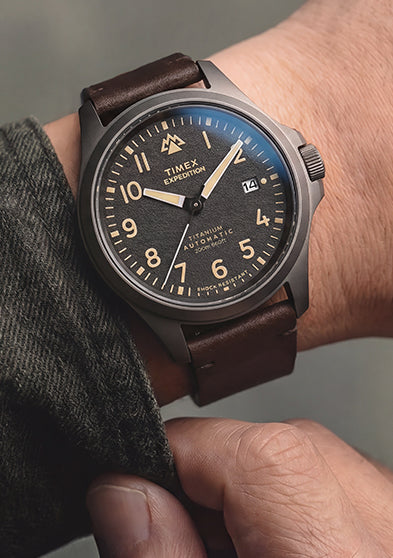 Expedition® Field Post Automatic titanium watch with a brown leather strap worn on the wrist, showcasing the black textured dial.