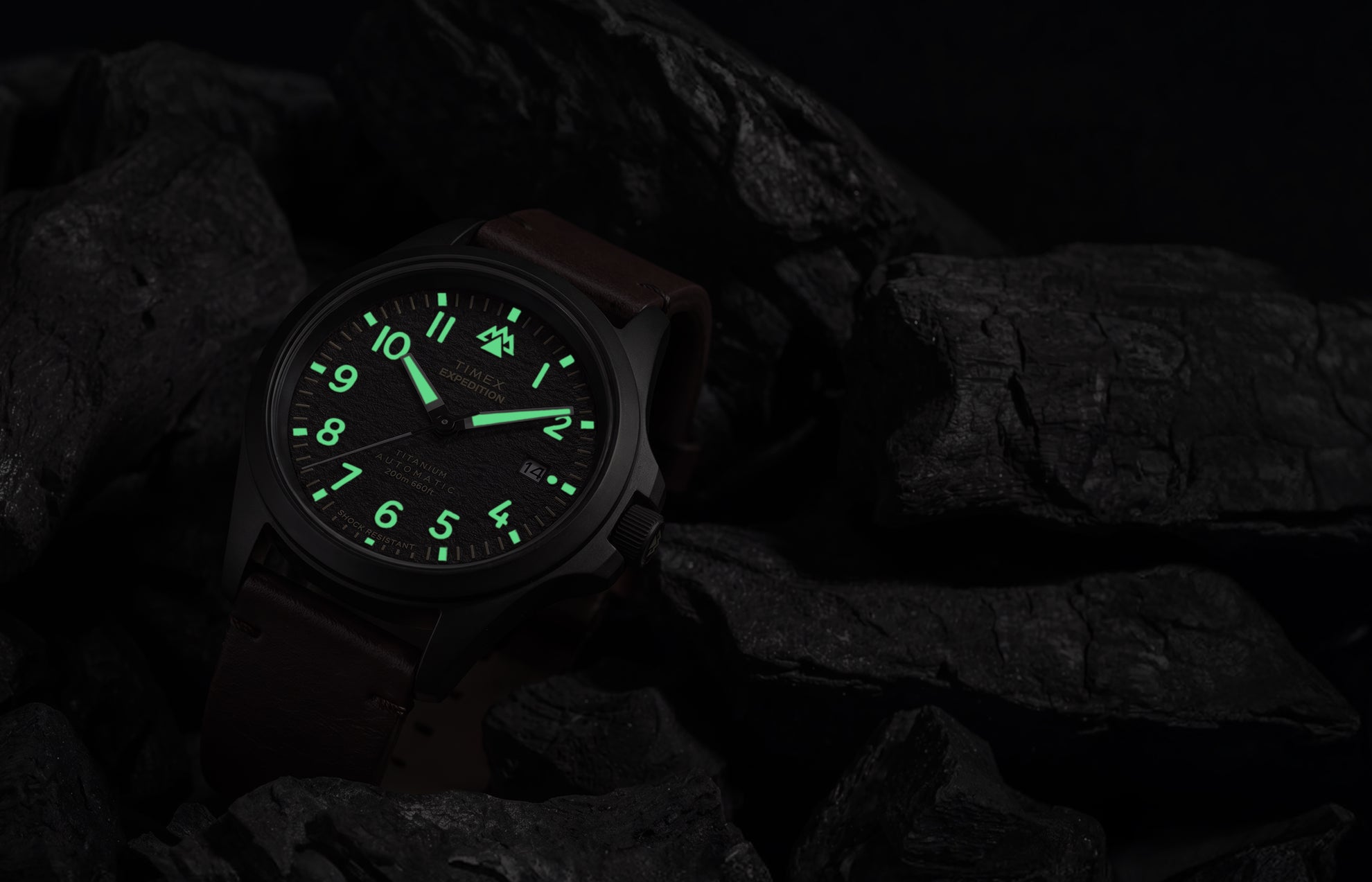Expedition® Field Post Automatic titanium watch with glowing luminous hands and hour markers in low light.