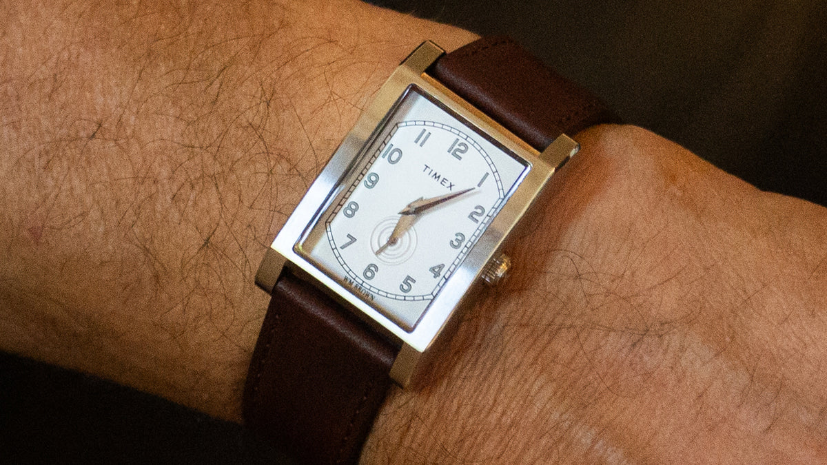 TWG069000 Primer plano de un reloj WM Brown x Timex en una muñeca, en el que se aprecian su esfera blanca, los números arábigos, la subesfera de los segundos y la correa de piel marrón.
