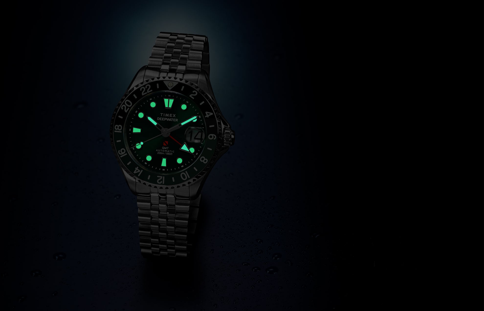 Timex Deepwater Meridian 200 Automatic GMT watch with a green dial and glowing luminous hands and hour markers, displayed against a dark blue background with water droplets.