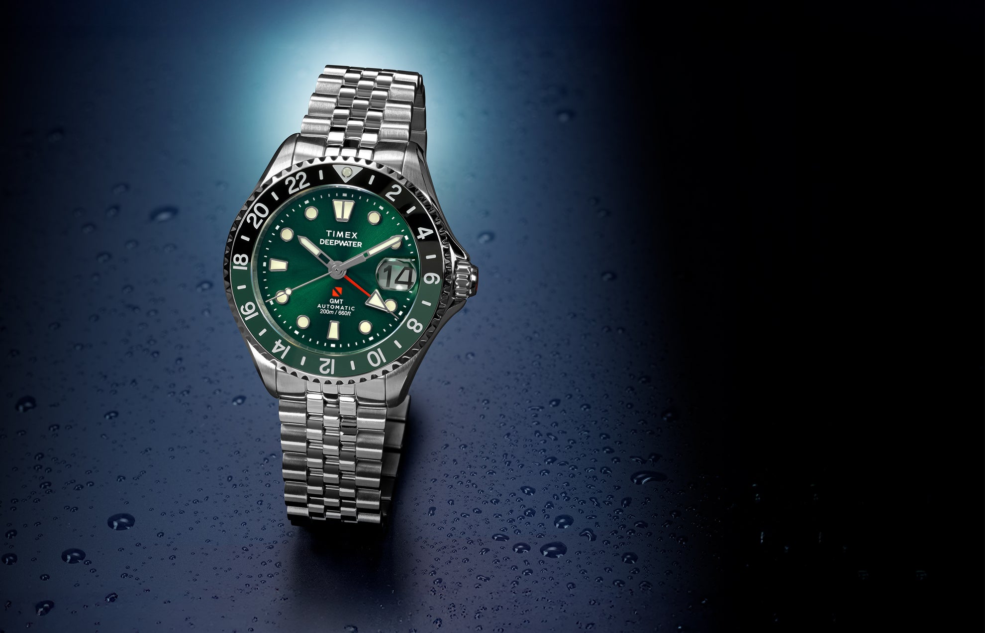 Timex Deepwater Meridian 200 Automatic GMT stainless steel watch featuring a green sunray dial, black-and-green GMT bezel, magnified date window, and jubilee-style bracelet on a water-droplet background.