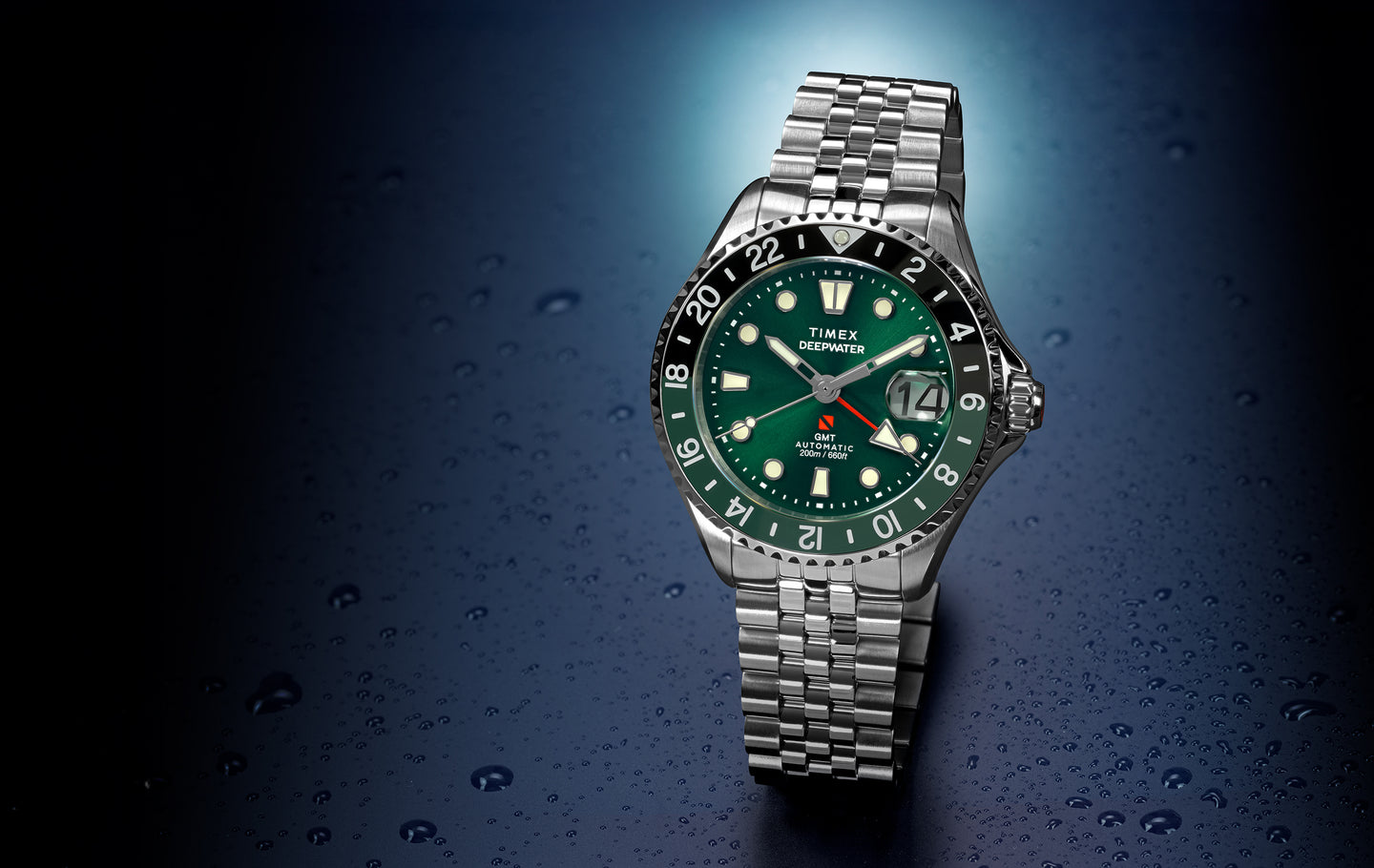 Deepwater Meridian 200 Automatic GMT watch with a green dial and matching green 24-hour GMT bezel, stainless steel case and jubilee-style bracelet, date magnifier at 3 o’clock, displayed against a dark blue water droplet background.