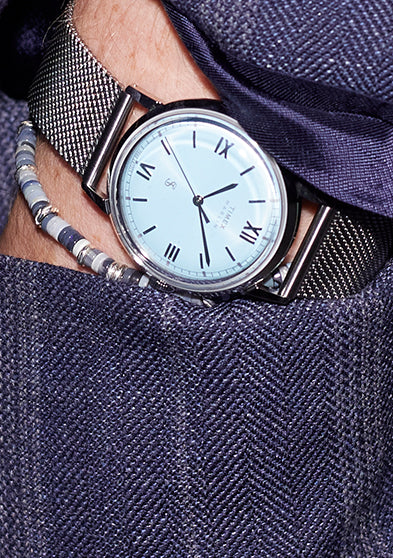 Todd Snyder x Timex Marlin® Mesh watch with a light blue dial tucked into the pocket of a navy pinstripe blazer, paired with beaded bracelets.