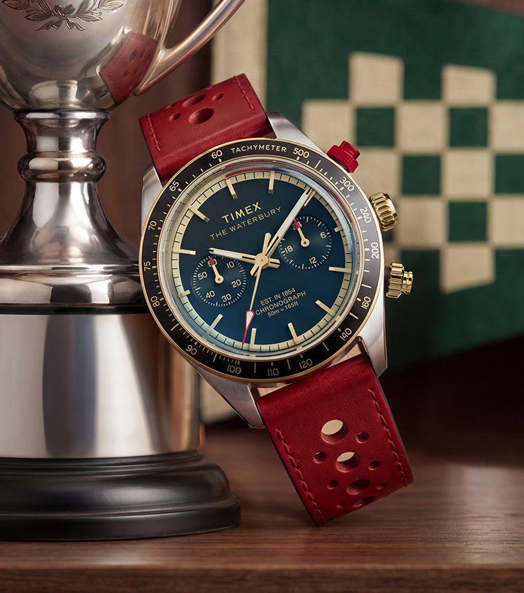 Waterbury Heritage Chronograph with blue dial and red leather strap displayed beside a silver trophy, with vintage racing-inspired decor in the background.