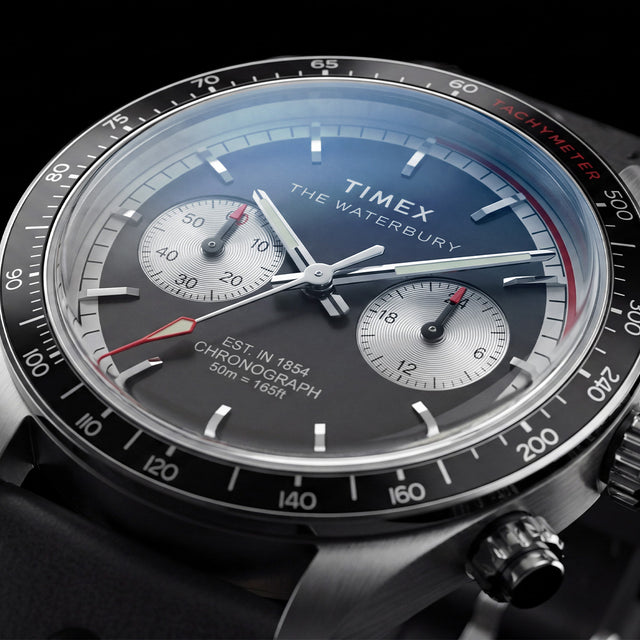 Close-up of the Timex Waterbury Heritage Chronograph featuring a black and silver panda-style dial, dual chronograph sub-dials, tachymeter bezel, and red chronograph accents.
