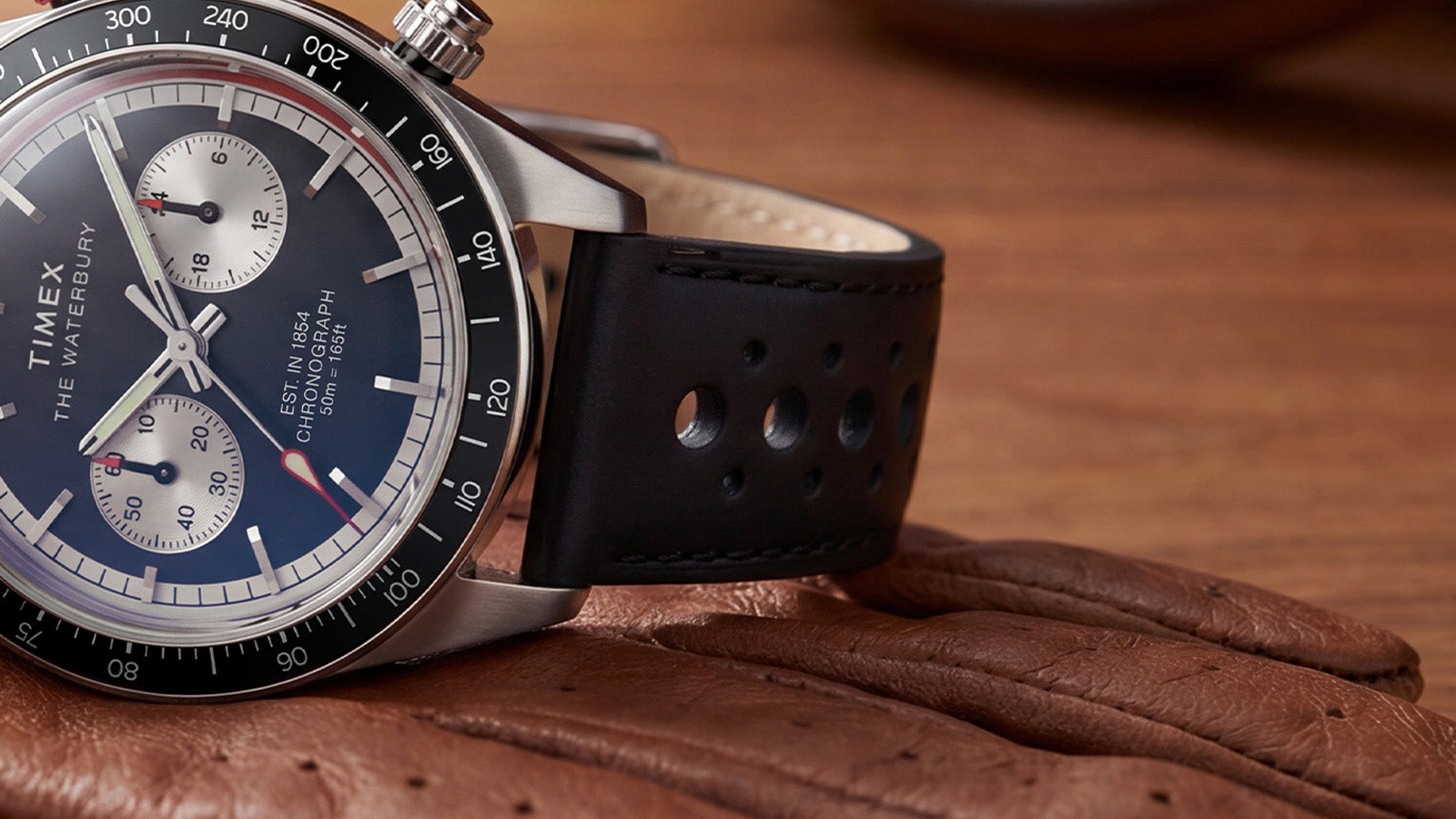Close-up of the Timex Waterbury Heritage Chronograph black perforated leather racing strap attached to the stainless steel case.