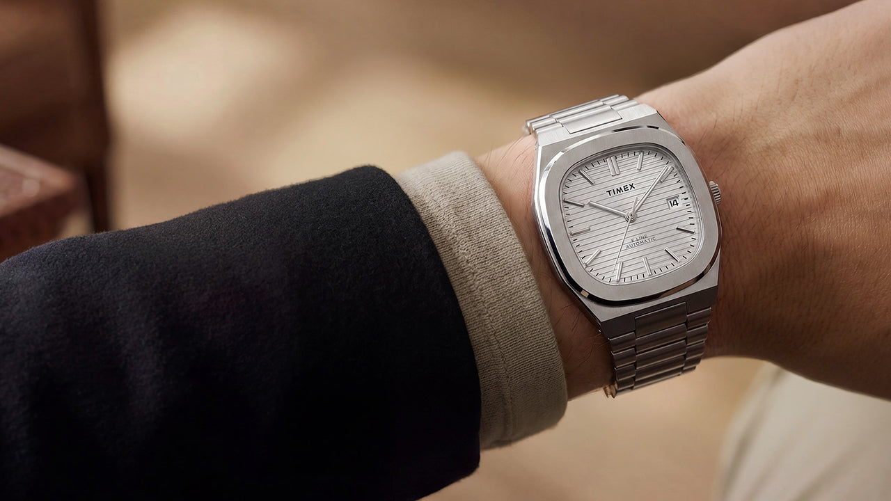 Primer plano del reloj Timex® Automatic E Line de 38 mm, de acero inoxidable, con esfera plateada texturizada y ventana de fecha, puesto en la muñeca.