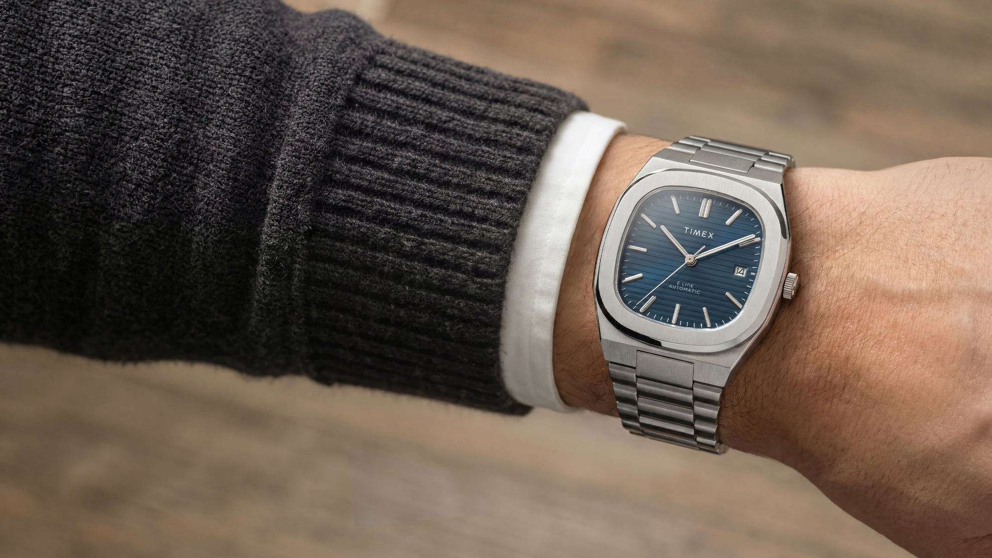 Primer plano del reloj Timex® Automatic E Line de 38 mm, de acero inoxidable, con esfera azul texturizada y ventana de fecha, puesto en la muñeca.