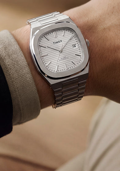 Primer plano del reloj Timex® Automatic E Line de 38 mm, de acero inoxidable, con esfera plateada texturizada y ventana de fecha, puesto en la muñeca.