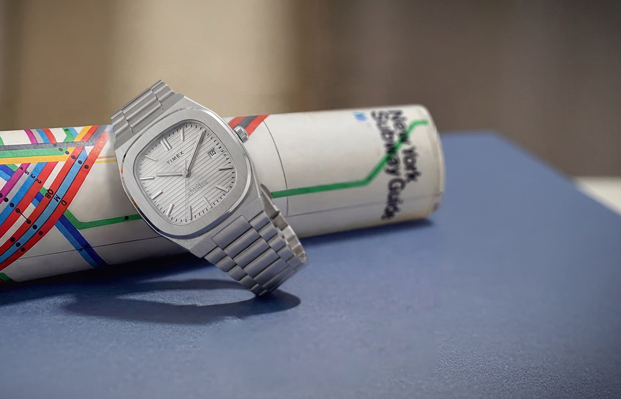 Timex Automatic E Line 38mm with a silver-tone dial and stainless-steel bracelet, displayed against a colorful transit map.