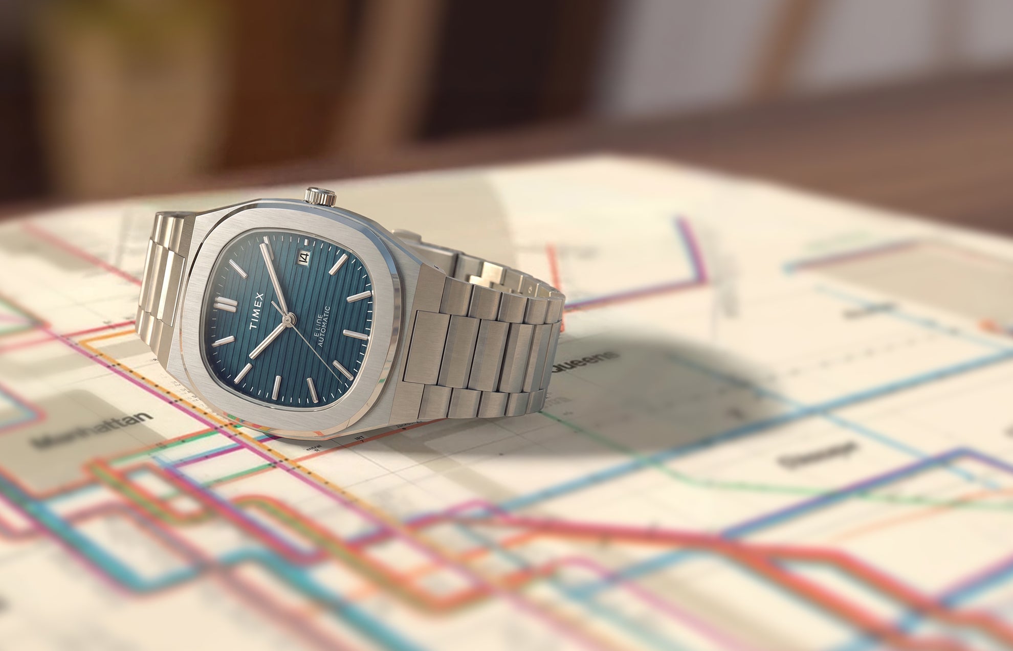 Timex Automatic E Line 38mm with a blue dial and stainless-steel bracelet, displayed on a colorful transit map.