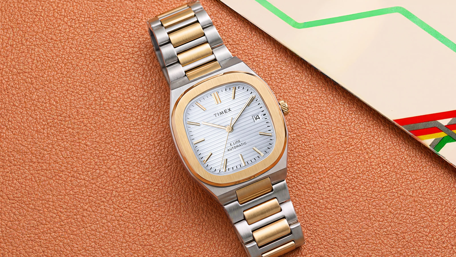 Timex® Automatic E Line 38mm two-tone stainless steel watch with a silver textured dial displayed beside a colorful transit map.