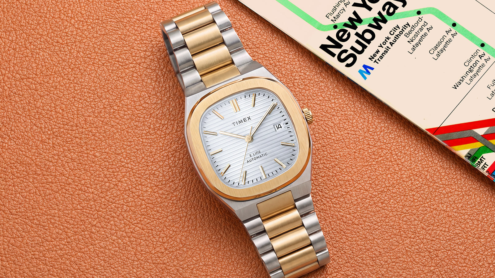 Timex® Automatic E Line watch with a silver dial and two-tone bracelet resting beside a New York subway map.