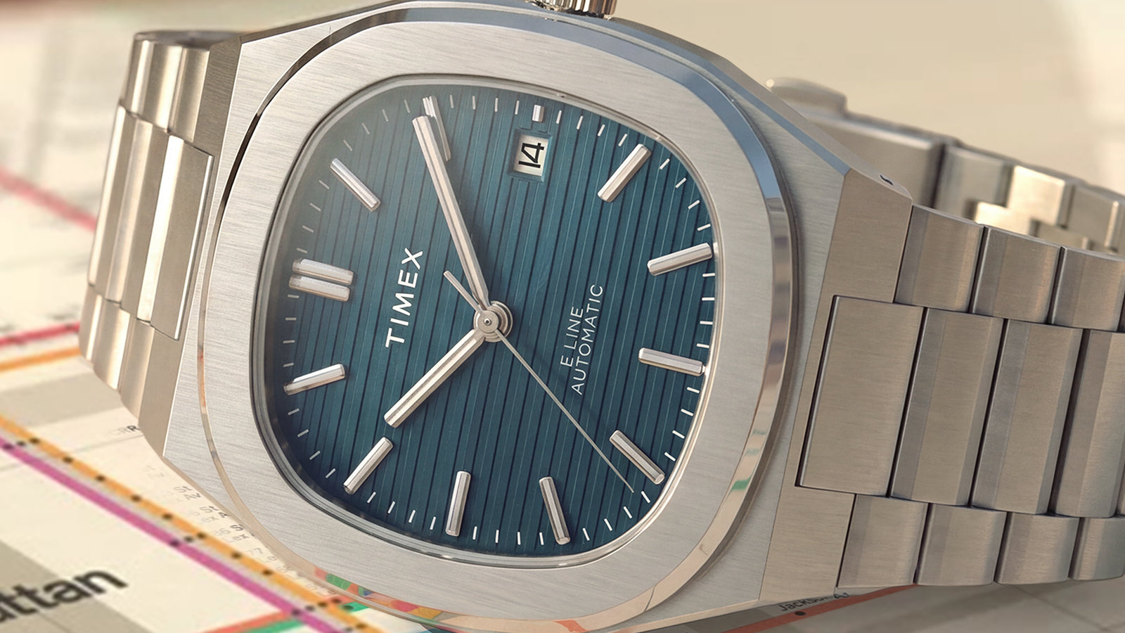 Primer plano del Timex® Automatic E Line de 38 mm, con una esfera azul con textura vertical, ventana de fecha, caja de acero inoxidable cepillado y brazalete integrado de acero inoxidable.