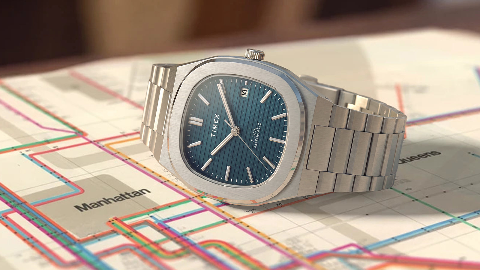 Reloj Timex® Automatic E Line de 38 mm, de acero inoxidable, con una esfera azul texturizada representada sobre un colorido mapa de transporte público.