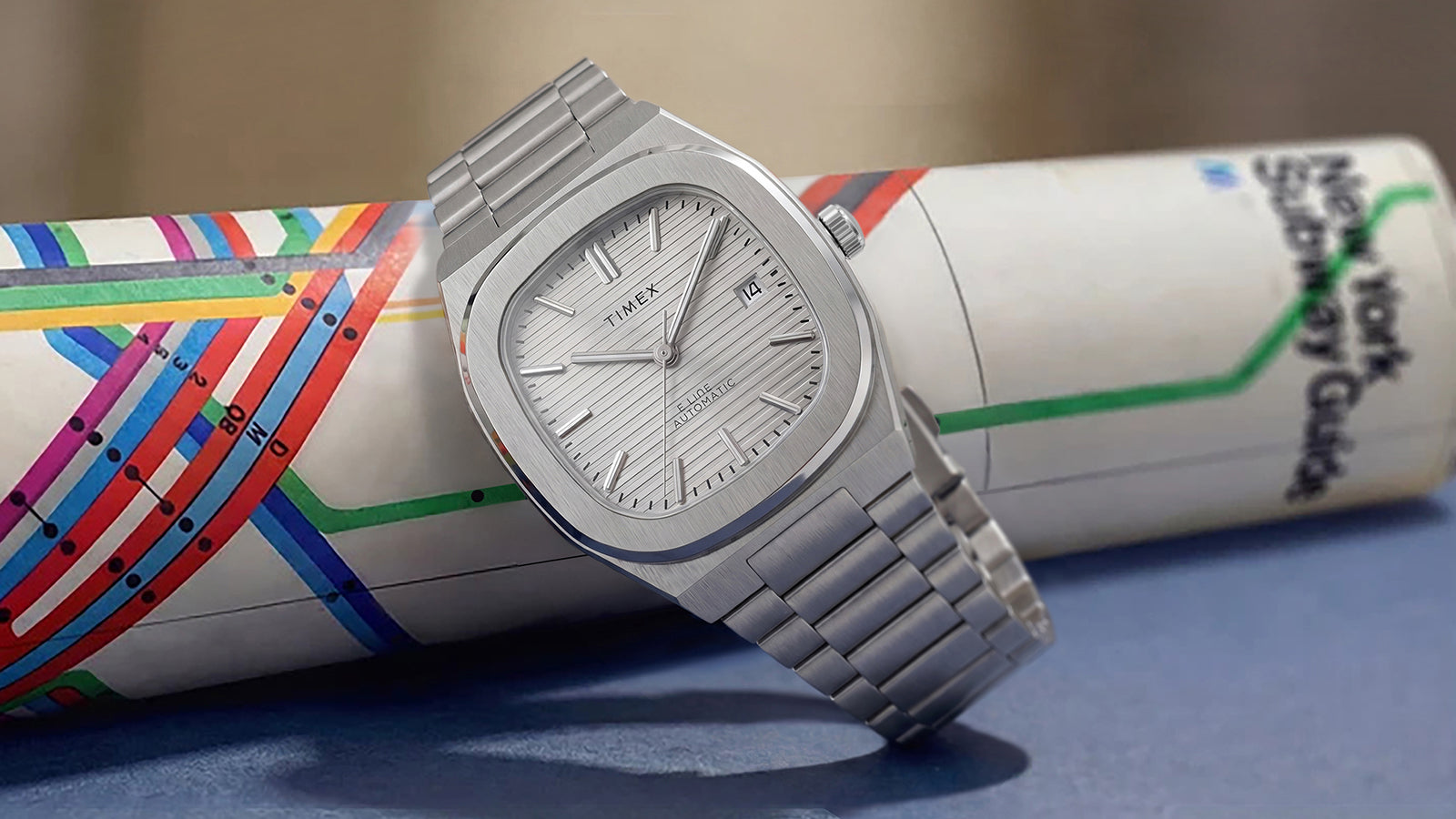 Timex Automatic E Line 38mm with a silver-tone dial and stainless-steel bracelet, displayed against a colorful transit map.
