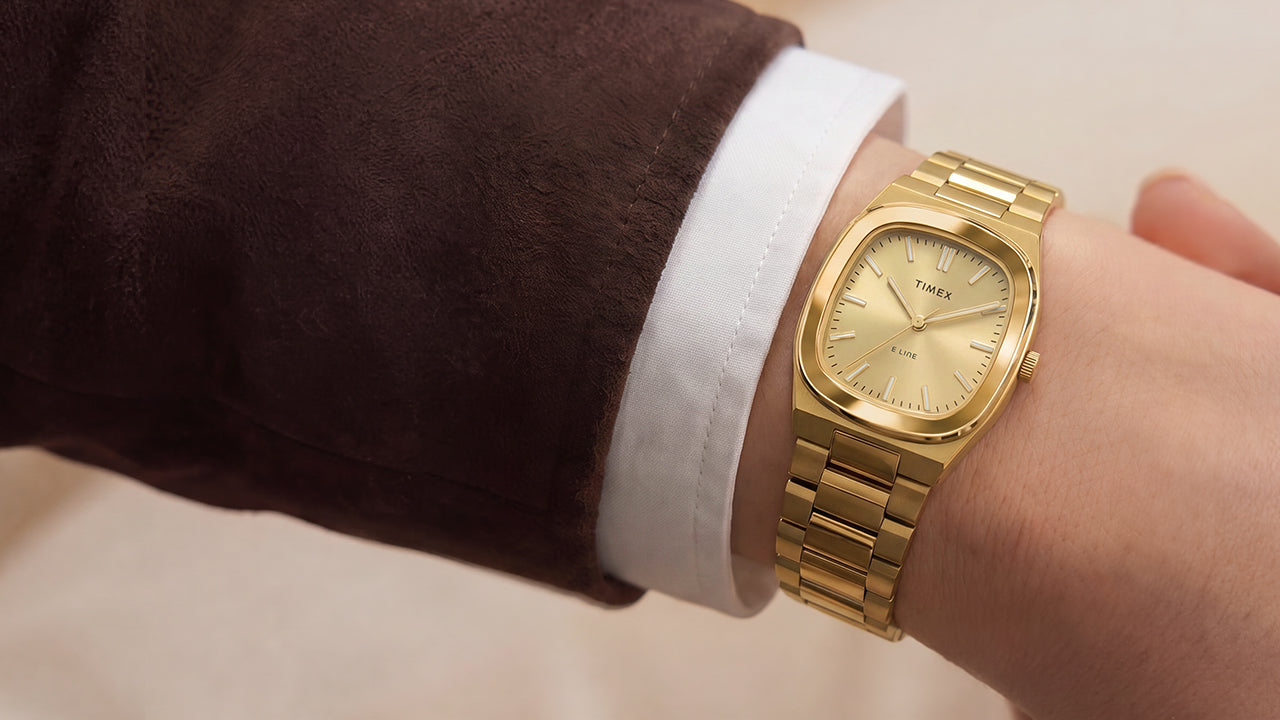 Primer plano del reloj Timex® Quartz E Line de 30 mm, de acero inoxidable en tono dorado y con esfera color champán, puesto en la muñeca.