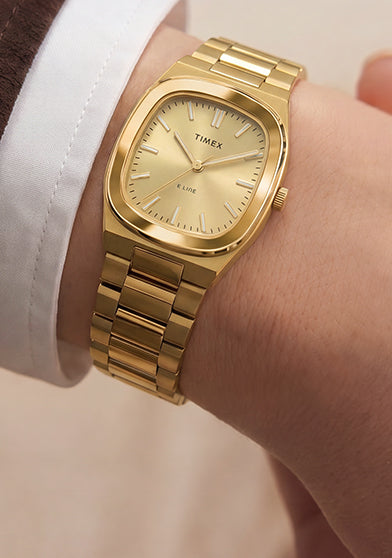 Primer plano del reloj Timex® Quartz E Line de 30 mm, de acero inoxidable en tono dorado y con esfera color champán, puesto en la muñeca.