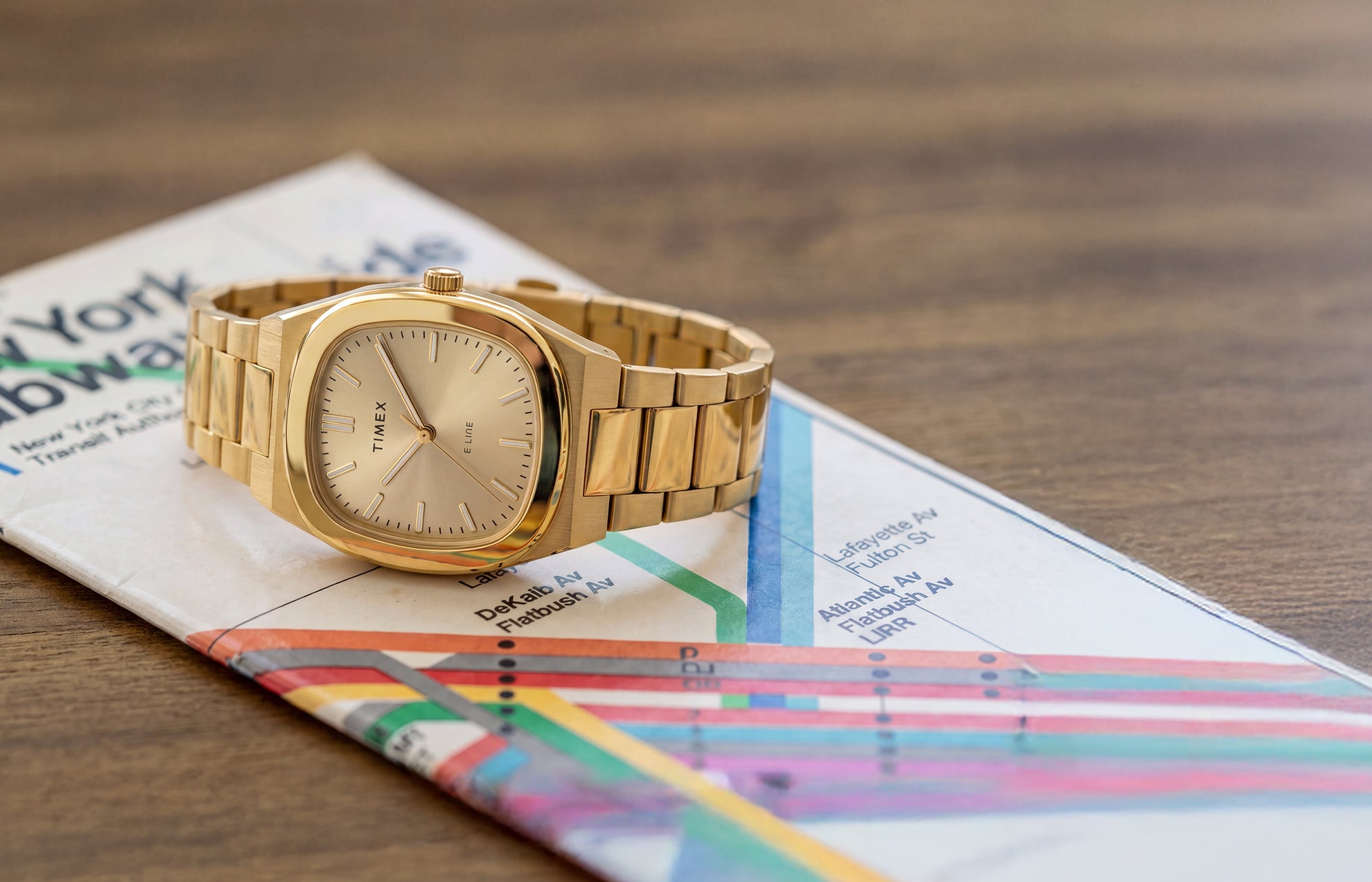 Reloj Timex® Quartz E Line de 30 mm con brazalete de acero inoxidable en tono dorado y esfera color champán, presentado sobre un mapa del metro de Nueva York.