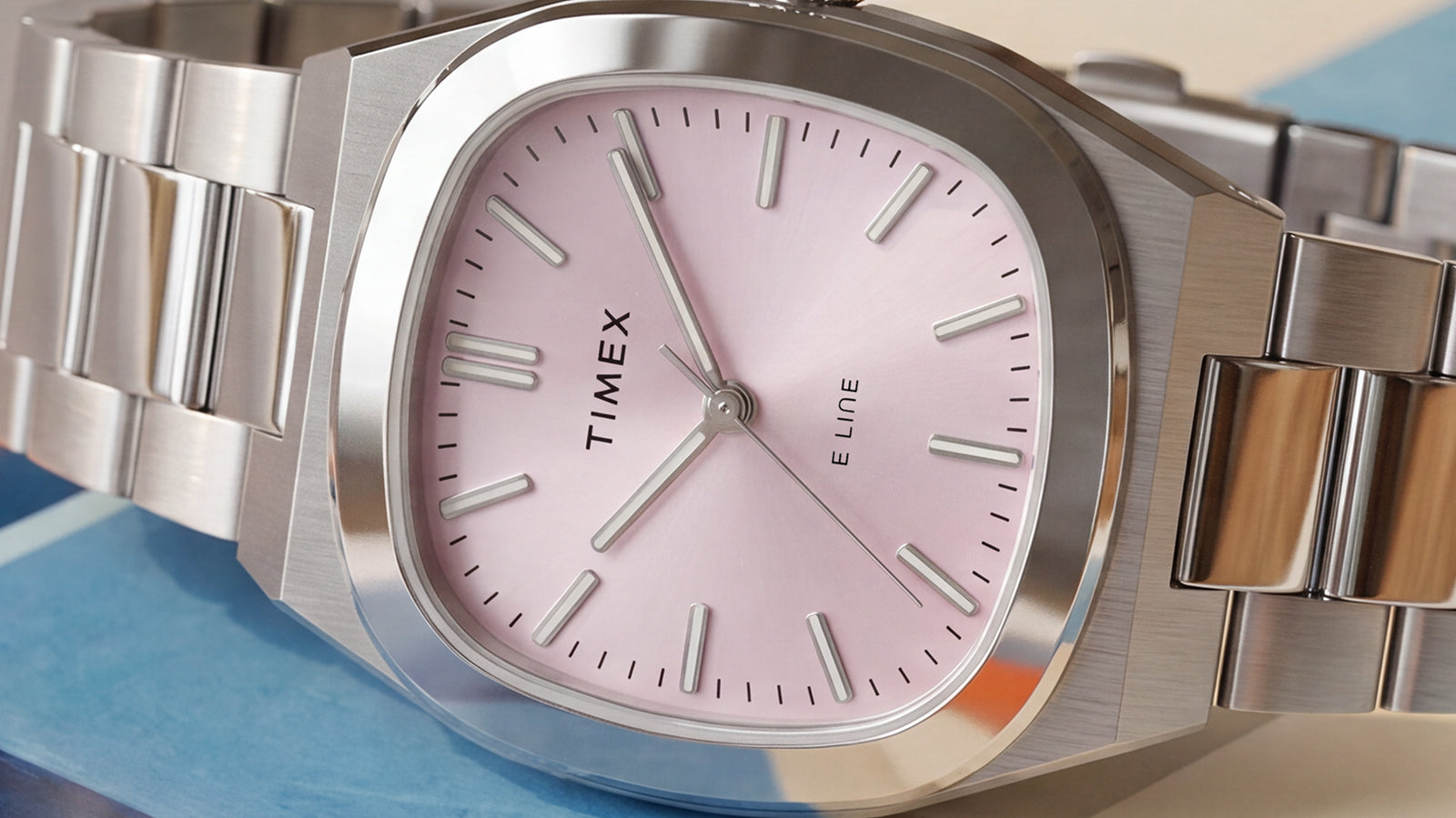 Primer plano del Timex® Quartz E Line de 30 mm, con una esfera rosa pálido con acabado rayos de sol, caja de acero inoxidable pulido y brazalete de acero inoxidable.