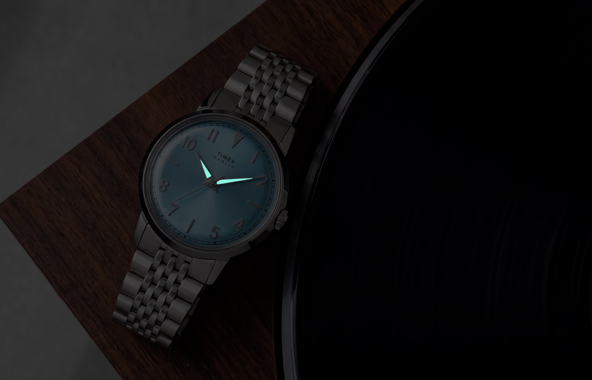 Timex Marlin Quartz watch with luminous hands glowing in low light beside a vinyl record.