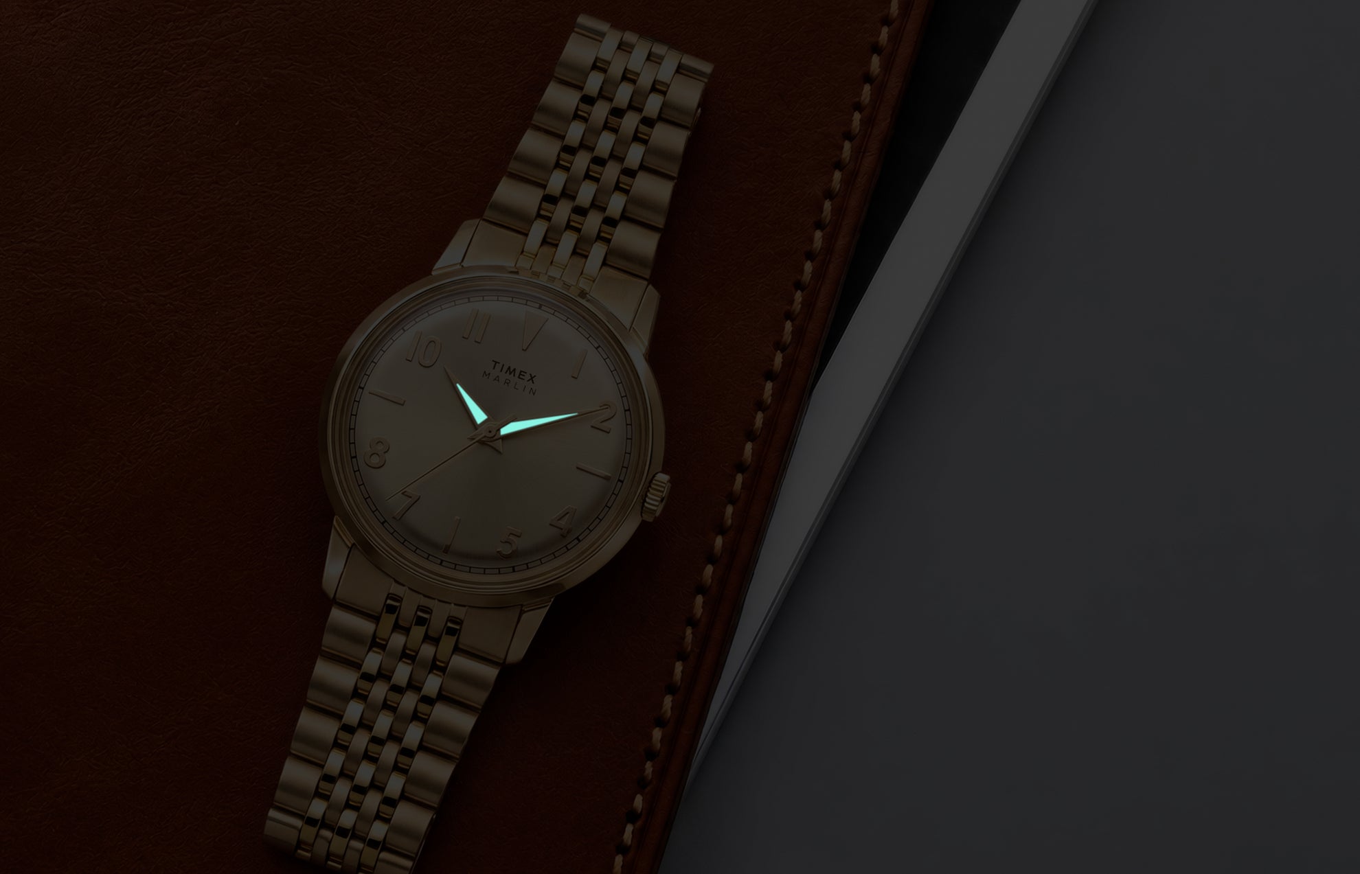 Timex Marlin Quartz watch with luminous hands glowing in low light against a champagne sunray dial.