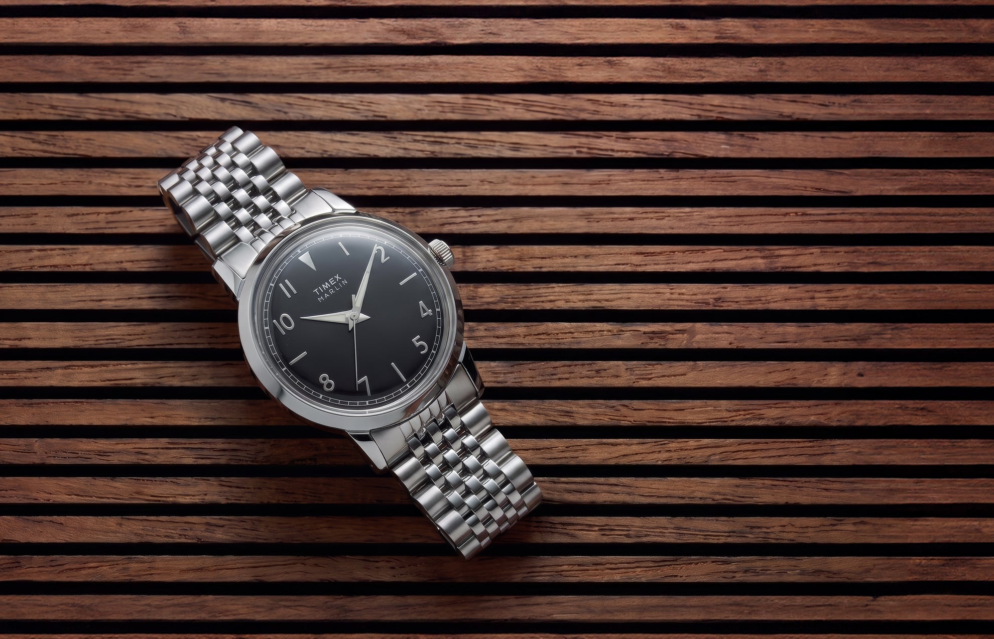 Timex Marlin Quartz watch with a black sunray dial and stainless steel bracelet displayed on a slatted wood surface.