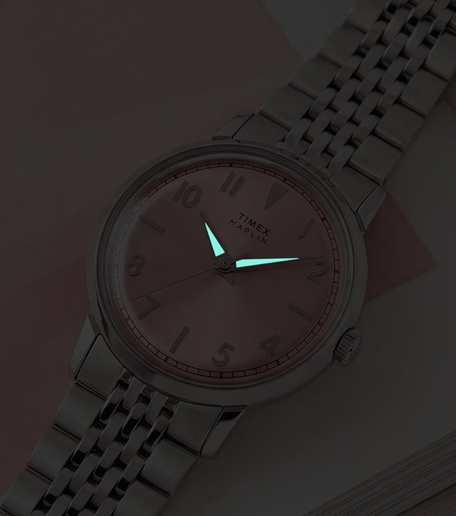 Timex Marlin Quartz watch with luminous hands glowing in low light against a pink sunray dial.