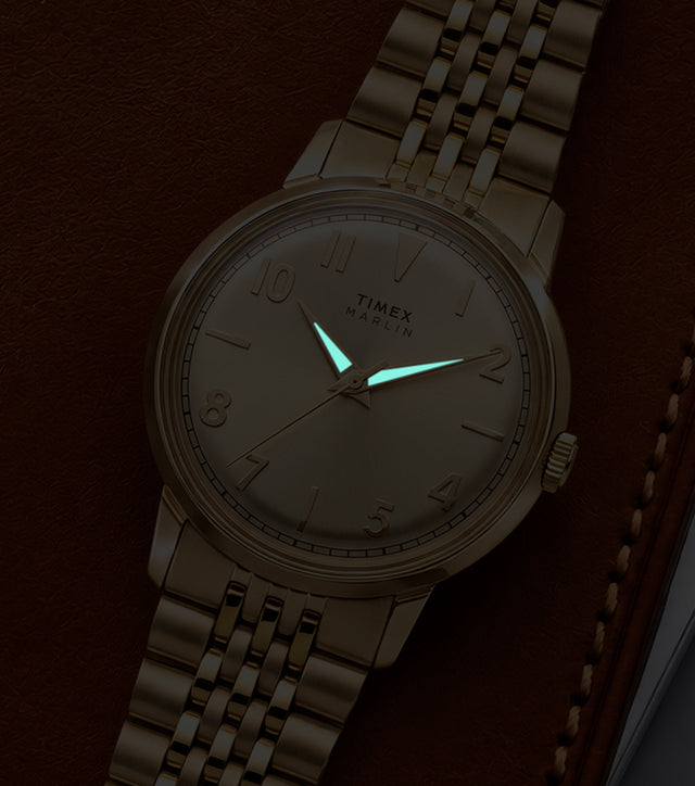 Timex Marlin Quartz watch with luminous hands glowing in low light against a champagne sunray dial.