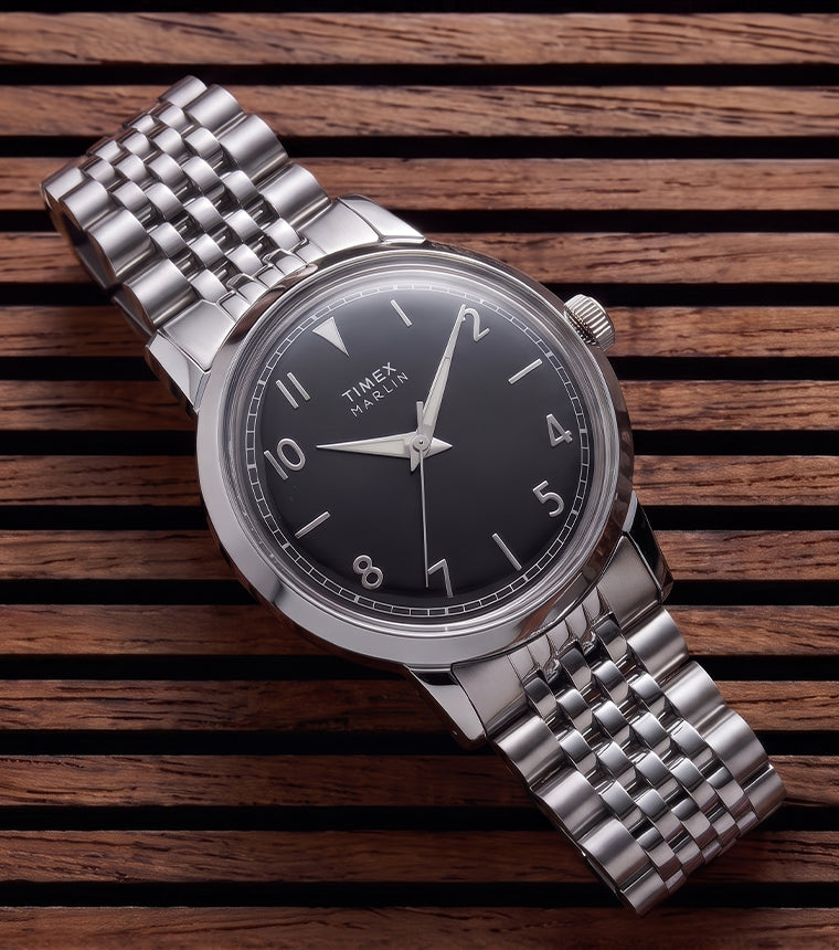Timex Marlin Quartz watch with a black sunray dial and stainless steel bracelet displayed on a slatted wood surface.