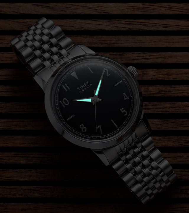 Close-up of the Timex Marlin Quartz with luminous hands illuminated on a black sunray dial in low light.