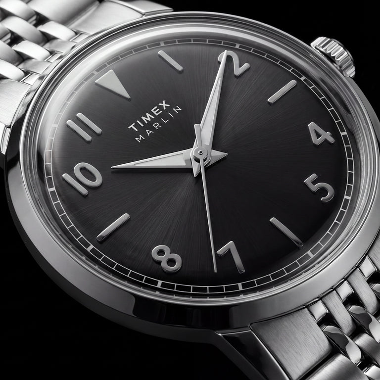 Macro view of the Timex Marlin Quartz black sunray dial with applied silver-tone Arabic numerals, luminous hands, and polished stainless steel case.