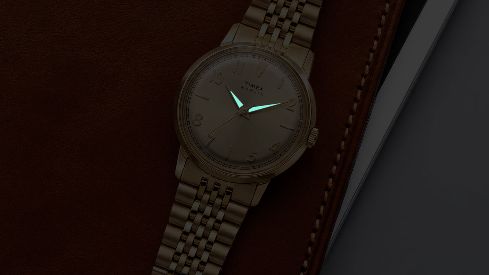 Close-up of the Timex Marlin Quartz with luminous hands illuminated on a champagne sunray dial in low light.