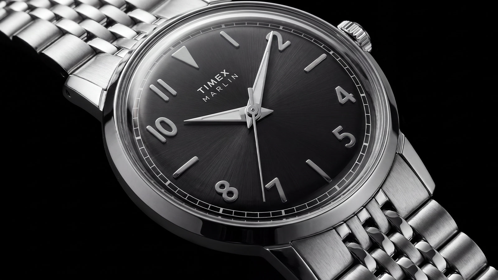Close-up of the Timex Marlin Quartz featuring a black sunray dial, applied silver-tone Arabic numerals, polished stainless steel case, and stainless steel bracelet.