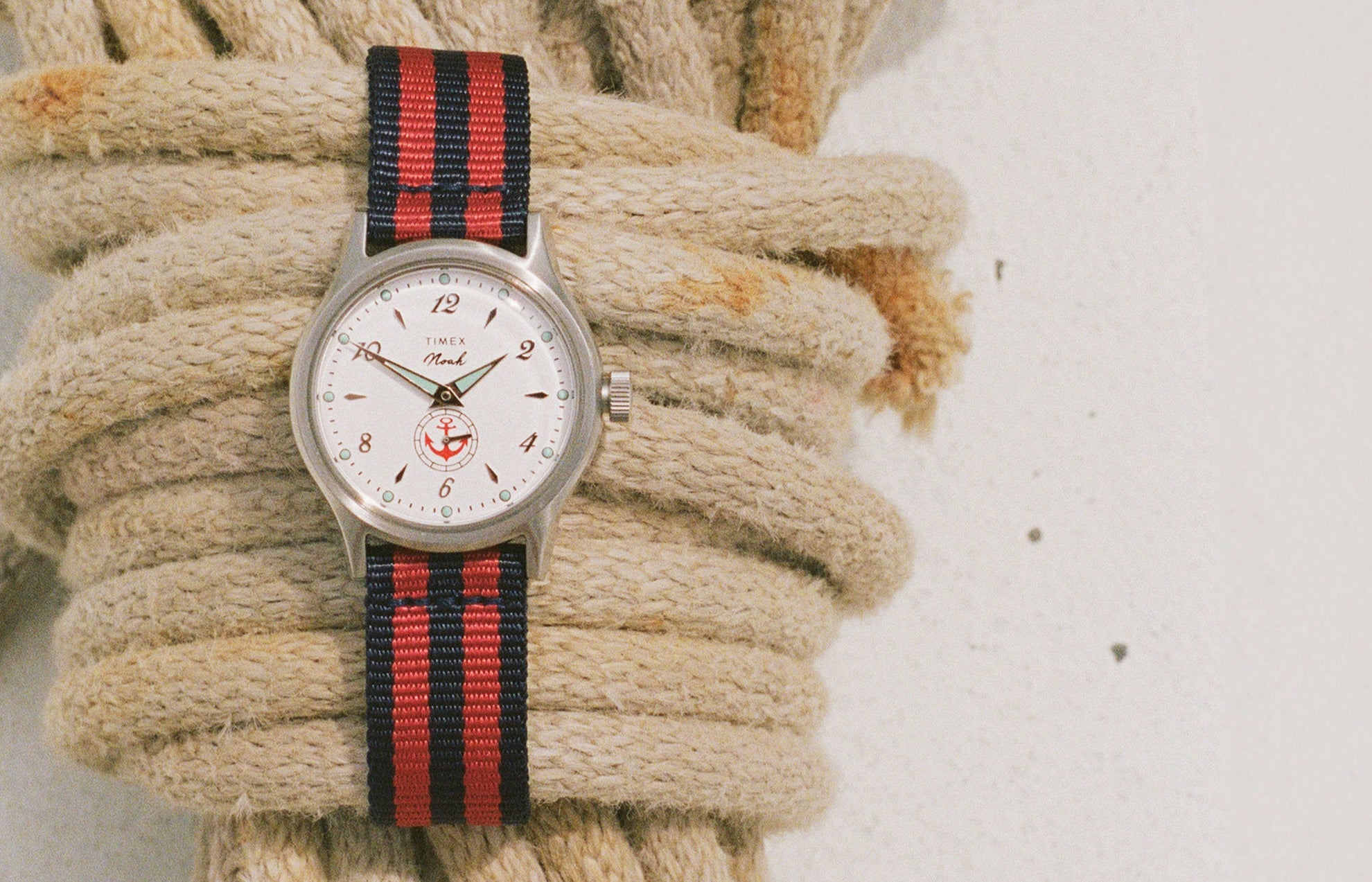 Reloj NOAH x Timex MK1 Anchor con esfera blanca y correa de tela a rayas rojas y azul marino, sujeta con una cuerda náutica trenzada.