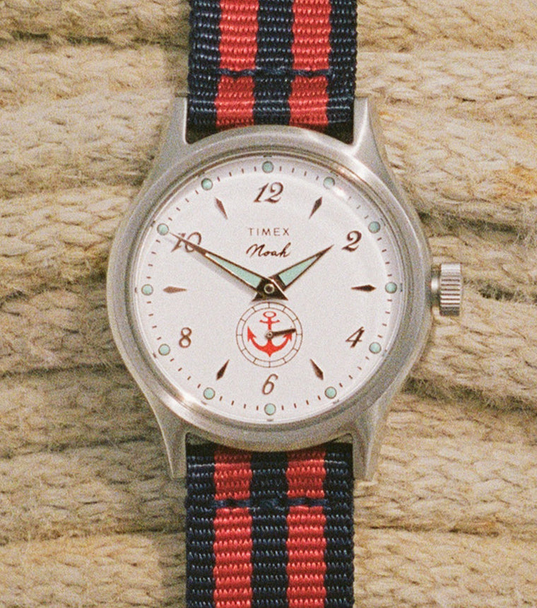 Reloj NOAH x Timex MK1 Anchor con esfera blanca y correa de tela a rayas rojas y azul marino, sujeta con una cuerda náutica trenzada.