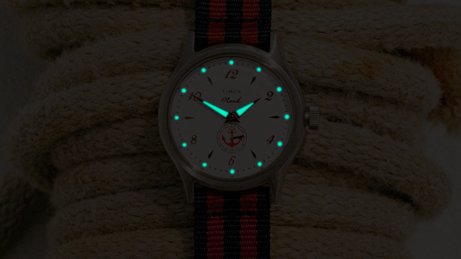 Primer plano del reloj NOAH x Timex MK1 Anchor, con agujas e índices luminosos que brillan en la oscuridad.