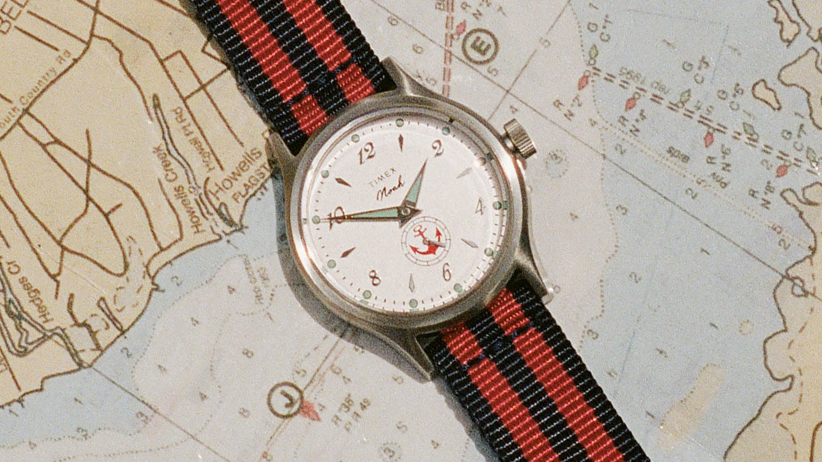 Reloj NOAH x Timex MK1 Anchor con esfera blanca y correa de tela a rayas colocada en diagonal sobre una carta náutica.