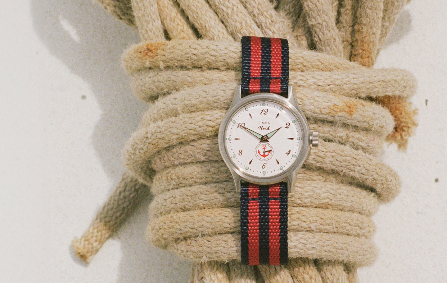 NOAH x Timex MK1 Anchor watch with a white dial and red-and-navy striped fabric strap resting on coiled nautical rope.