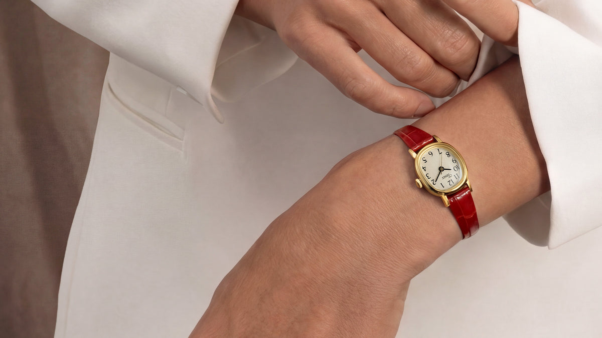 Cavatina® Mini watch with a gold-tone case and red leather strap worn on a wrist with a white outfit.