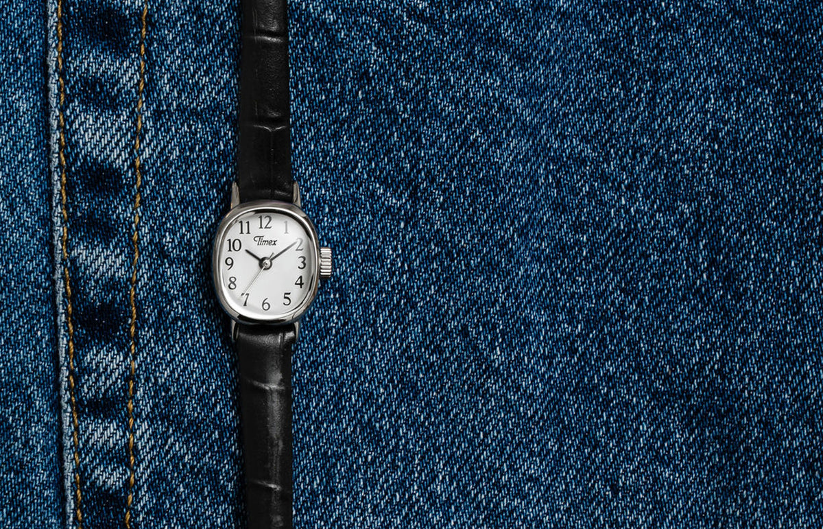 Cavatina® Mini watch with a silver-tone case, white dial, and black leather strap displayed on blue denim.